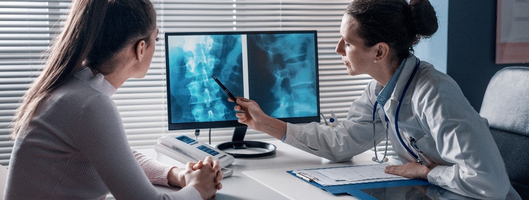 Arzt erklärt Patient etwas an Röntgenbild der Wirbelsäule